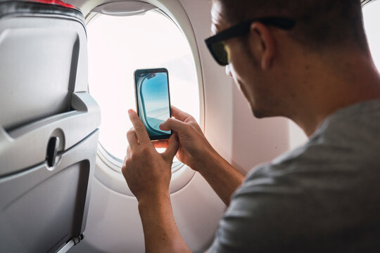 Man in airplane, using smartphone, taking a picture, airplane window