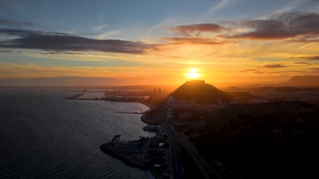 Alicante al atardecer desde el mar con el sol detr&aacute;s del Castillo de Santa Barbara , panor&aacute;mica a&eacute;rea