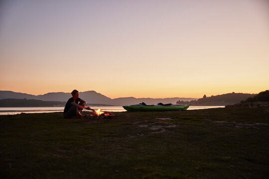 Chile, Talca, Maule River, woman sitting at camp fire beside canoe