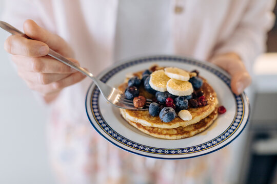 Close-up of woman holding a plate with pancakes and fruit