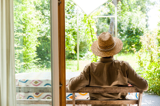 Back view of senior man wearing straw hat on terrace enjoying his garden