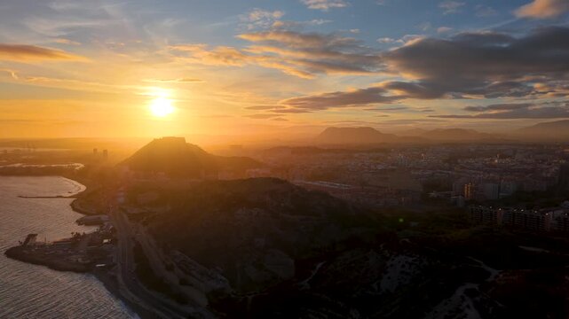 Alicante al atardecer desde el mar con el sol detr&aacute;s del Castillo de Santa Barbara , panor&aacute;mica a&eacute;rea