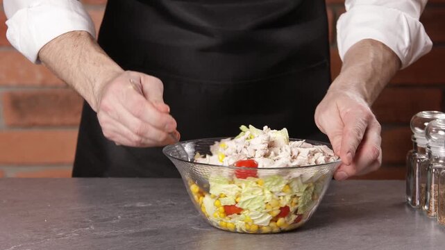 The cook stirs the tomato, cabbage and corn salad in a bowl with a spoon.