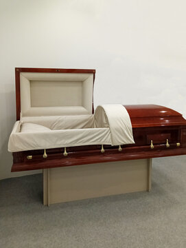 Polished red wooden coffin with white satin trim, open lid, and brass handles, displayed on stand. Elite Grob manufactures  coffin in Kurganinsk