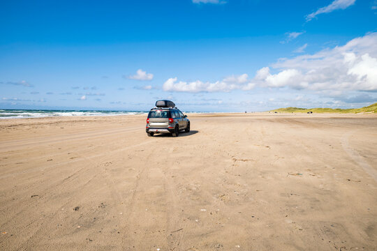 SUV on expansive sandy Saltum Strand beach in Denmark under blue sky
