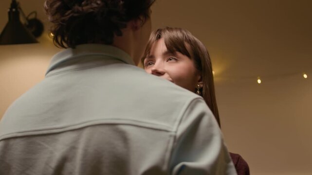 Medium close up shot of intimate young couple looking at each other and smiling while dancing together at home