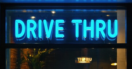 Obraz premium Bright neon sign displays Drive Thru. Dark background emphasizes glowing blue text. Nighttime scene, possibly restaurant exterior.