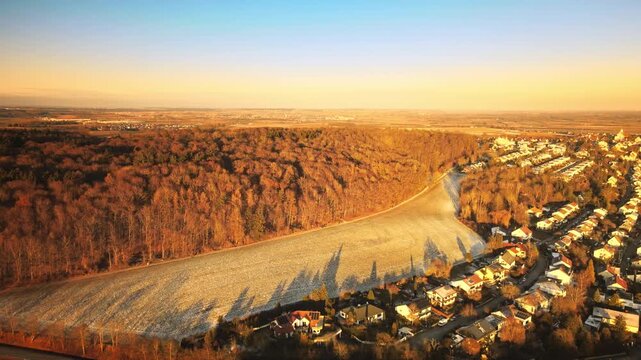 Forward-moving drone at golden hour near Elchingen, gliding over rolling frosty fields and expansive forest landscape with warm sunset light and long shadows.