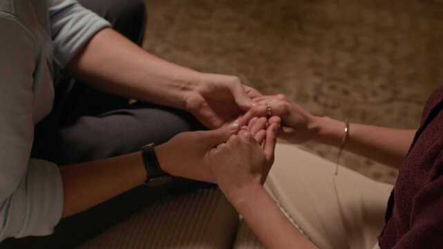 Close up shot of anonymous man and woman holding their hands while sharing intimate moment sitting on home sofa under warm light
