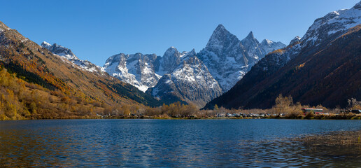 Tumanly Kel lake against of high rocky snow-capped mountains and forested slopes