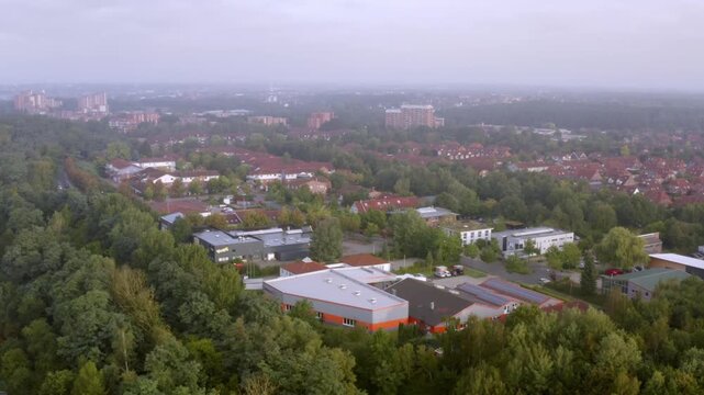 Aerial view of a L&uuml;neburg commercial and residential area. The foreground features functional flat buildings with green roofs and solar panels, surrounded by dense trees and housing estates.