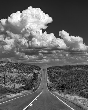 USA, Idaho, Fairfield, Cumulus clouds over empty road crossing landscape, black and white