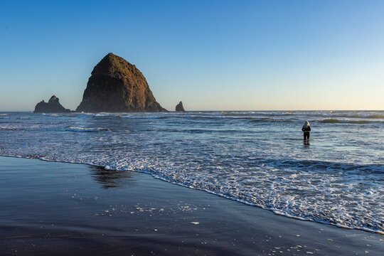 USA, Oregon, Cannon Beach, Rear view of woman wading in surf near haystack rock