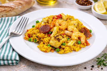 Paella aux crevettes, chorizo et l&eacute;gumes servie dans une assiette blanche