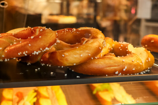 Close up of golden brown pretzels sprinkled with salt granules, ready for sale in a glass display case at a Parisian bakery