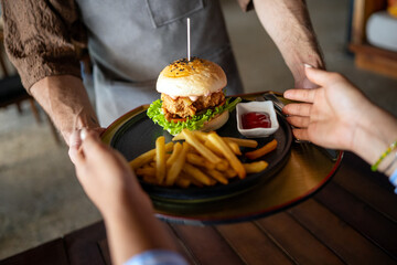 Casual dining lifestyle, waiter serves a delicious burger and fries in a relaxed restaurant setting