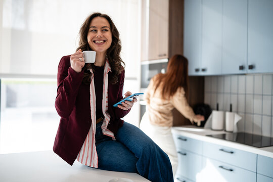 Woman enjoying coffee break using smartphone in kitchen