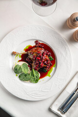 Duck confit leg served with rich berry sauce and greens on elegant white plate