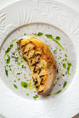 Grilled cabbage steak served with creamy mushroom sauce and herb oil on elegant white plate