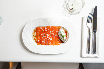 Fresh salmon slices served with creamy sauce fresh herbs and olive oil on elegant white plate