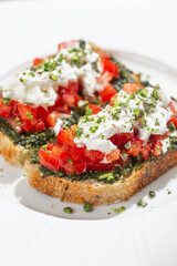 Toasted bread topped with basil pesto fresh tomatoes creamy burrata and herbs served on white plate