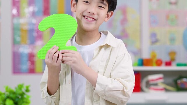 Smiling Child Holding Foam Number Two in Classroom