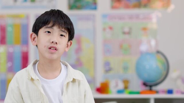 Asian schoolboy gesturing quiet sign in colorful classroom