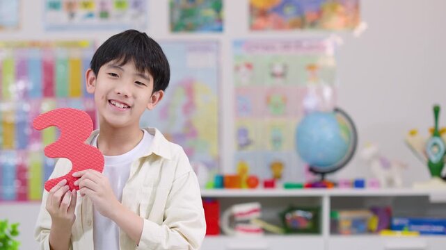 Smiling Boy Holding Foam Number Three in Classroom