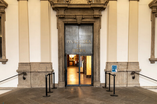 Entrance of Pinacoteca di Brera in Milan, Italy Front entrance of the Pinacoteca di Brera art museum with stone portal, signage, and queue stanchions, showing a warm interior glimpse through the open 