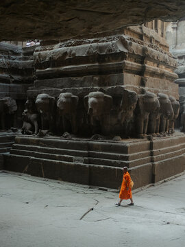 Verul, India - 27 December 2025: View of a monk in saffron robes walking across the courtyard of the Kailasa Temple, its monolithic rock carvings casting long shadows on the stone floor.