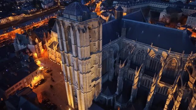 Cath&eacute;drale Saint-Julien du Mans illuminated at night, with glowing city lights of Le Mans in background, France. Aerial backward tilt-up reveal