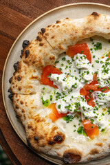 Italian style pizza topped with smoked salmon ricotta cheese and fresh chives served on wooden table