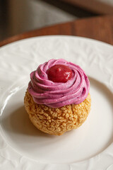 Choux pastry dessert filled and topped with raspberry cream served on elegant white plate
