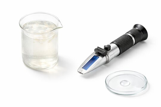 Clear glass beaker filled with coconut water with handheld refractometer and watch glass droplet laboratory quality testing studio photo isolated on white