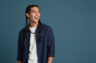 Fototapeta premium Cheerful Young Man with Braids Laughing Against a Blue Backdrop, Expressing Joy and Happiness, Looking Sideways