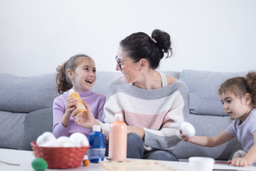 Mother and two daughters painting Easter eggs at home