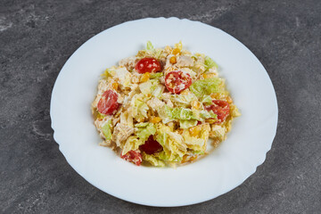 A ready-made salad of cabbage, corn, tomatoes and chicken breast with sauce on a white plate.
