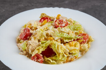 A ready-made salad of cabbage, corn, tomatoes and chicken breast with sauce on a white plate.