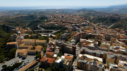 Fototapeta premium Panoramic aerial view of the city of Catanzaro, capital of the Calabria region in southern Italy. In the foreground are the town's houses, buildings, and rooftops. The Ionian Sea is on the horizon.