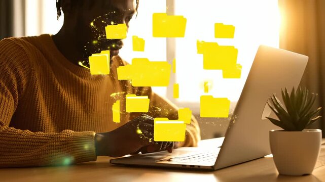 Man works on laptop with floating digital folder icons in home office. Virtual folders appear while typing on laptop. Man uses computer with digital folders. Working with virtual file system on laptop
