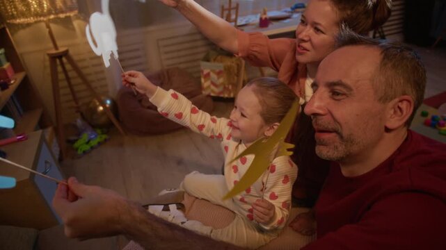 Caucasian family resting on floor and enjoying shadow puppets, they looking at wall with shadows and chatting