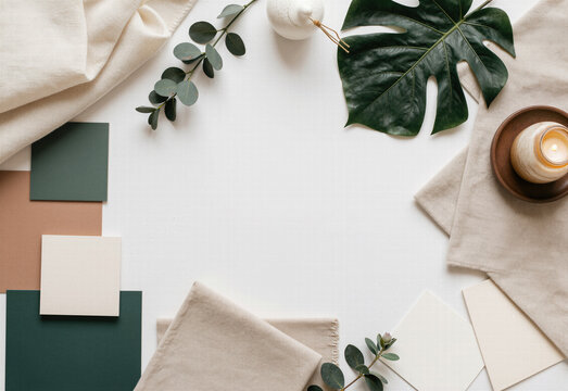Interior design mood board flat lay on white surface containing tropical monstera leaves eucalyptus and neutral fabric swatches with ceramic color tiles.
