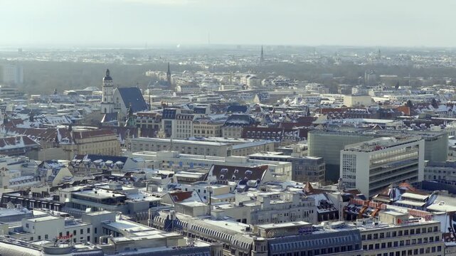 Industrial Leipzig in winter: A view over snow-covered rooftops and the power plant with smoking chimneys. In the background, wind turbines complete the panorama under a clear sky.