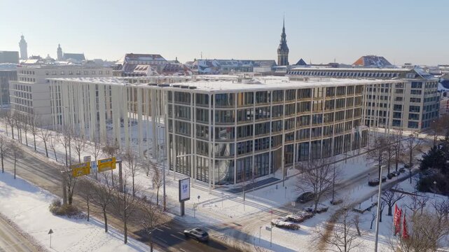 Modern architecture SAB Bank in snowy Leipzig: The glass office building on Dittrichring stands in contrast to the historic spire of St. Thomas Church under a clear winter sky.