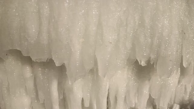 Close-up, Camera panning left side along icicles hanging from the roof. Winter scene with continuous hanging ice. Natural pattern of icing on sunny winter day.