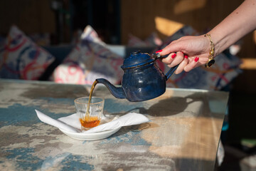 Nalewanie herbaty z czajniczka do szklanki – zbliżenie na rękę, słoneczny dzień © siwyk