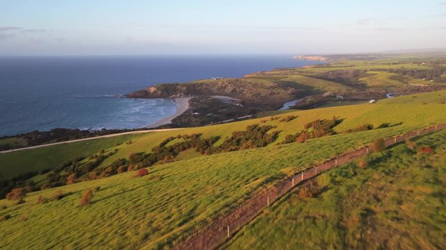 Epic sunset aerial flying over a black container home, revealing green rolling coastal hills and beach landscapes in Kangaroo Island, Australia, a popular travel destination in the South Pacific.