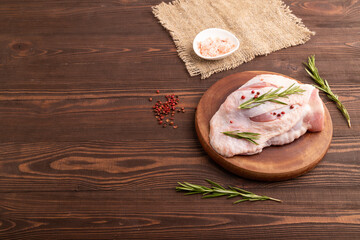 Raw Turkey Thigh with spices on cutting board on brown wooden, linen textile. side view, copy space
