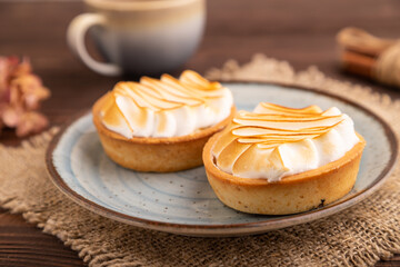 French lemon tart with meringue on brown wooden, linen textile, side view, close up, selective focus