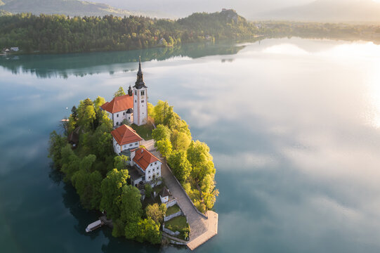 Aerial view of the serene island church, its white walls reflecting in the tranquil lake waters, a spiritual haven embraced by lush greenery, Bled, Radovljica, Slovenia.